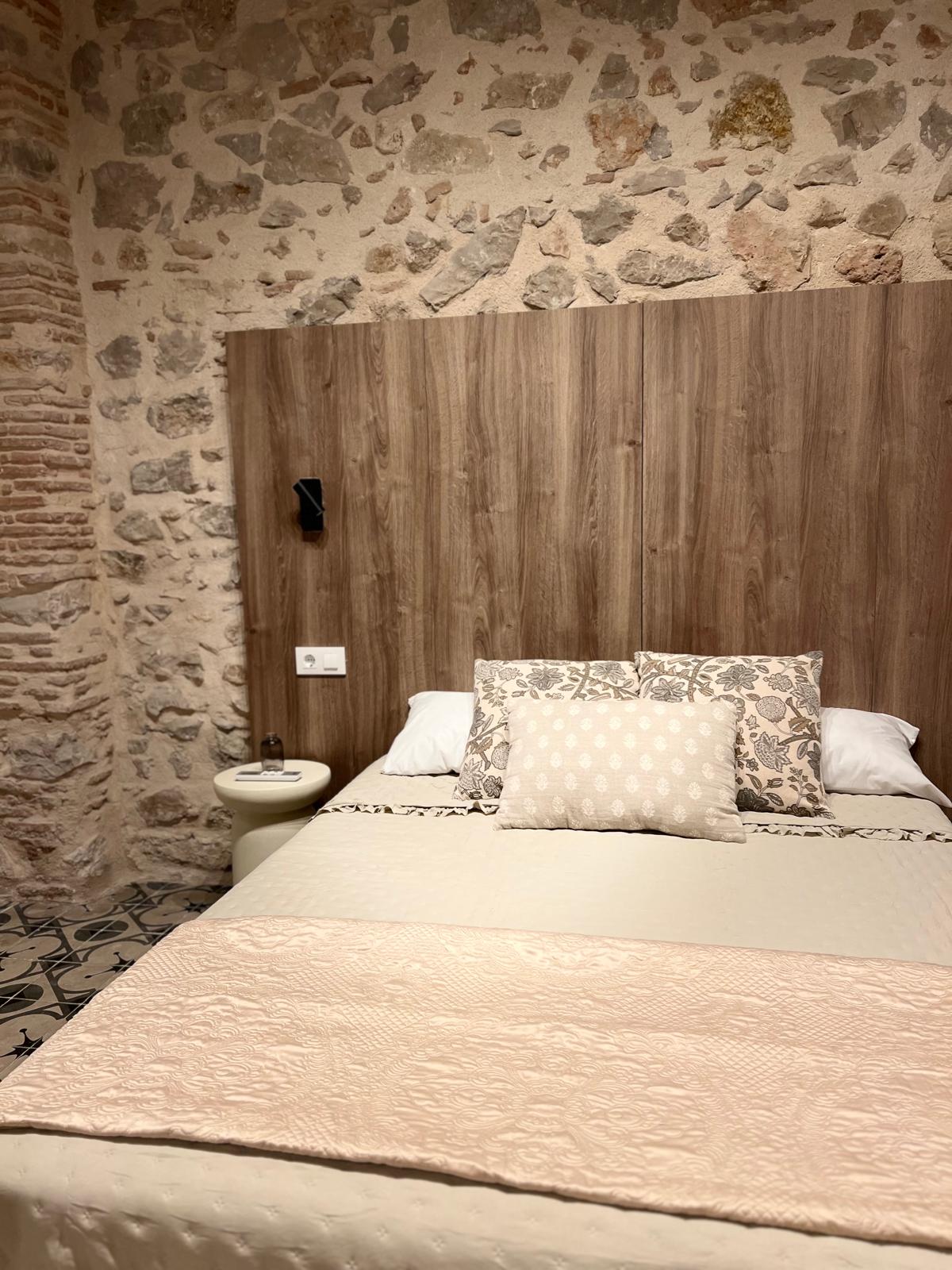 Dormitorio con cabecero de madera y pared de piedra - Casa rural Xeresa cerca Gandía
