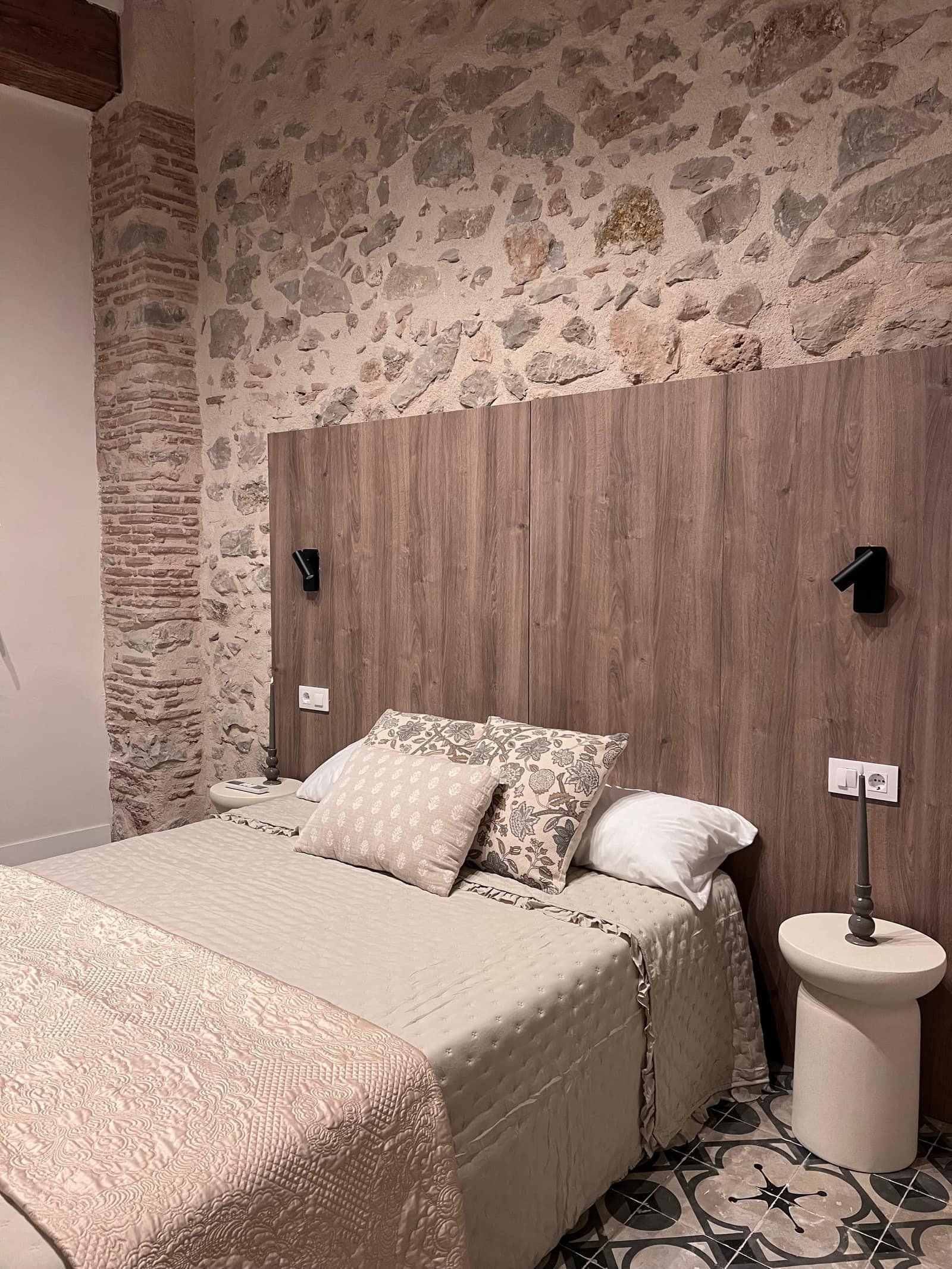 Dormitorio con cabecero de madera, pared de piedra y suelo hidráulico - Casa Filo Xeresa