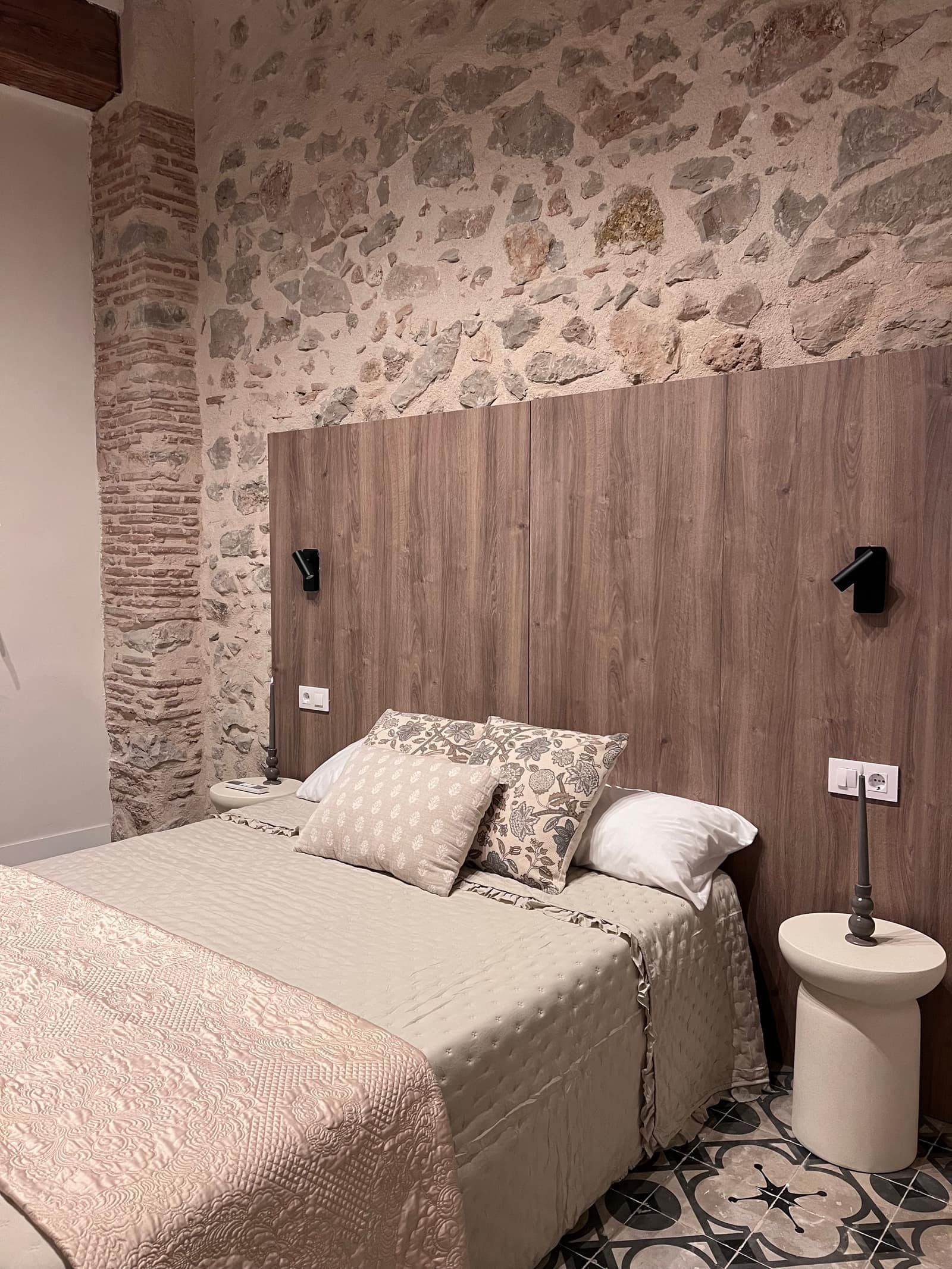 Dormitorio con cabecero de madera, pared de piedra y suelo hidraulico - Casa Filo Xeresa