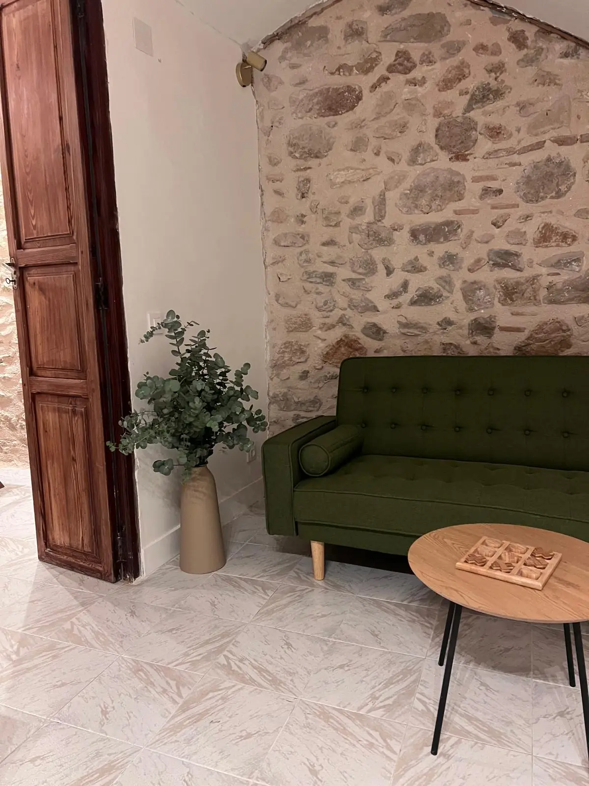 Salon con sofa verde y pared de piedra - Casa Filo Xeresa